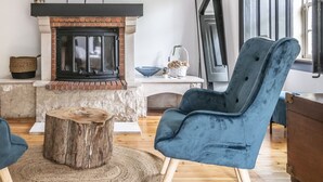 A cozy living room with a stone fireplace, two blue velvet chairs, a wooden coffee table, and a rustic side table. - Quinta dos Lobos Boutique Hotel - Nature Experience (Sintra)