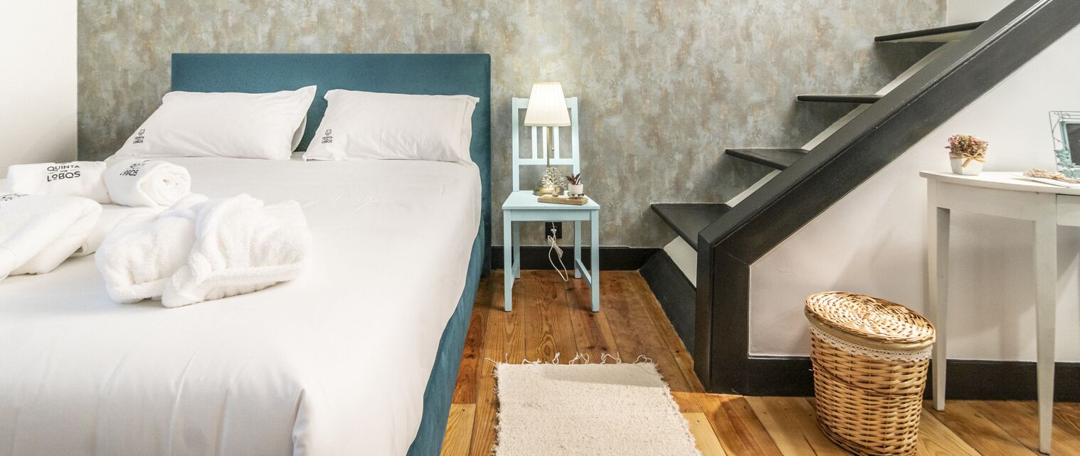 A hotel room with a bed, a nightstand, a lamp, a wicker basket, and a staircase.