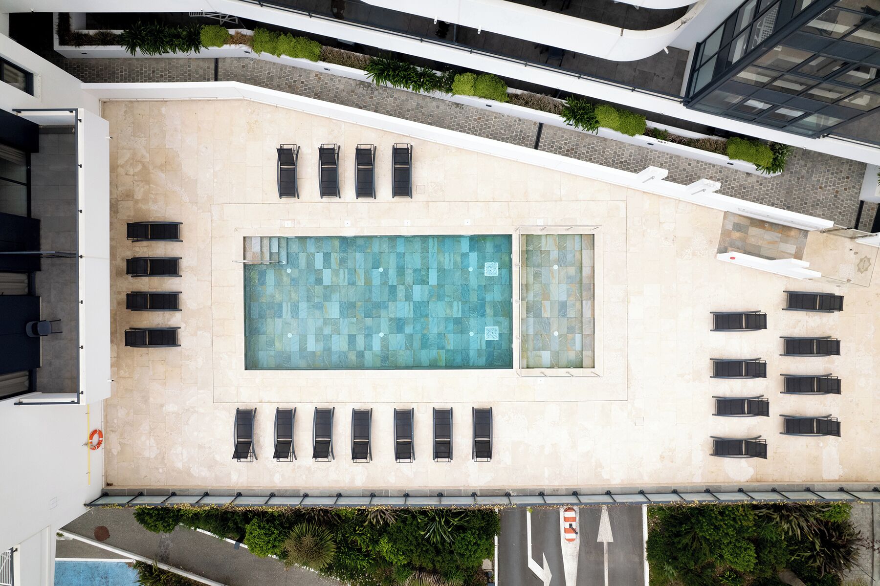 Vista aérea de un edificio con piscina en la azotea, varias sillas de descanso y un cielo despejado.