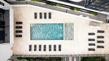 Vista aérea de un edificio con piscina en la azotea, varias sillas de descanso y un cielo despejado.