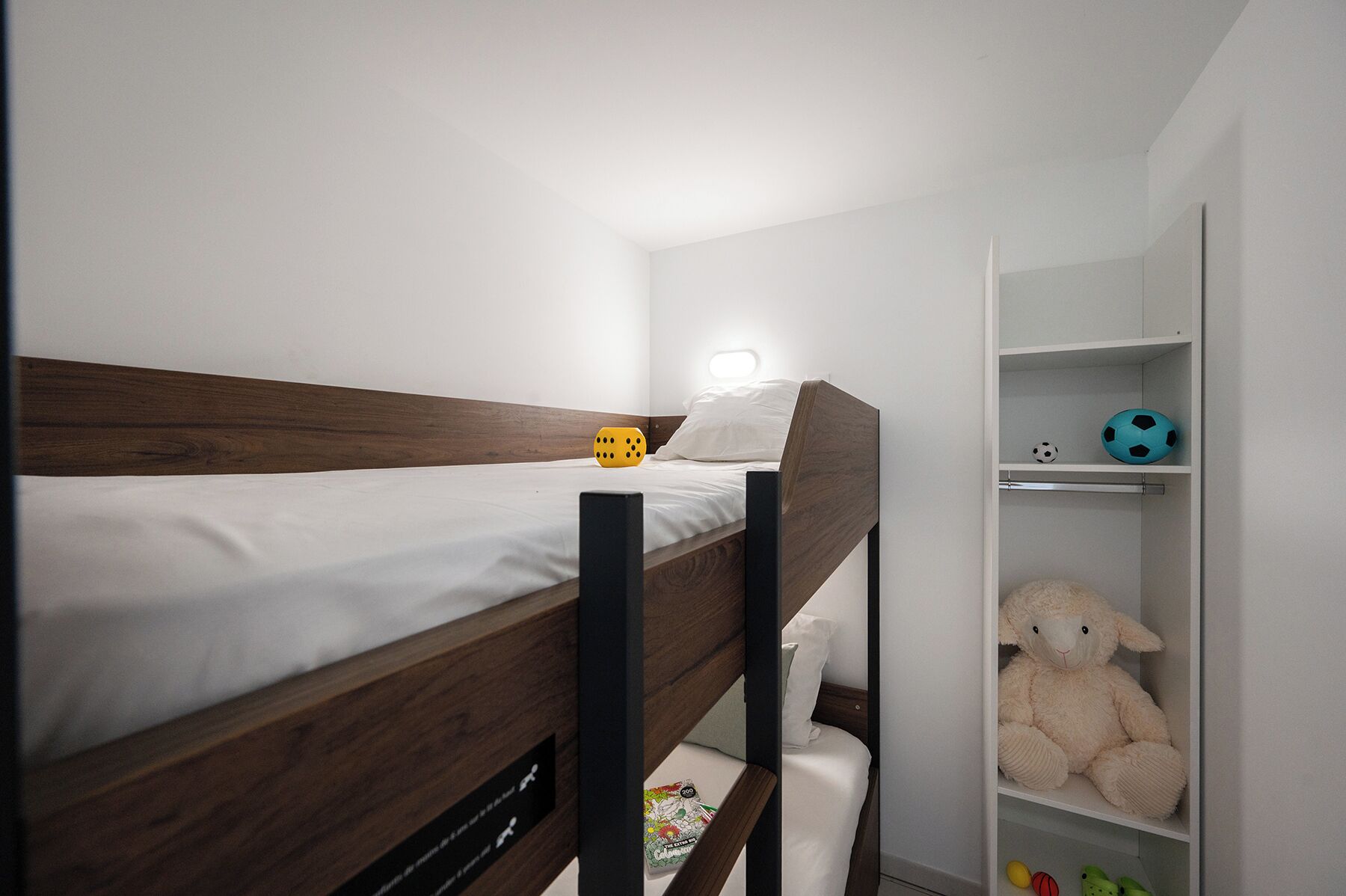 Ein Etagenbett mit Holzkopfstück, ein Nachttisch und ein Regal mit Stofftier und Fußball.