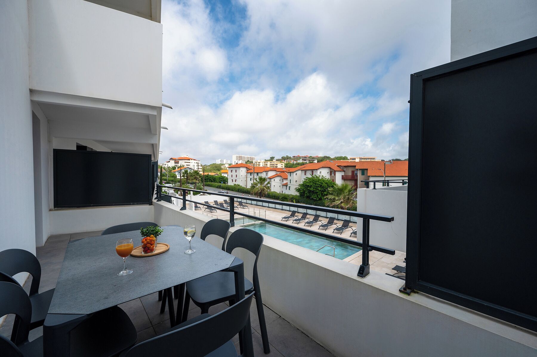 A balcony with a table and chairs, a pool, and a view of buildings in the background.
