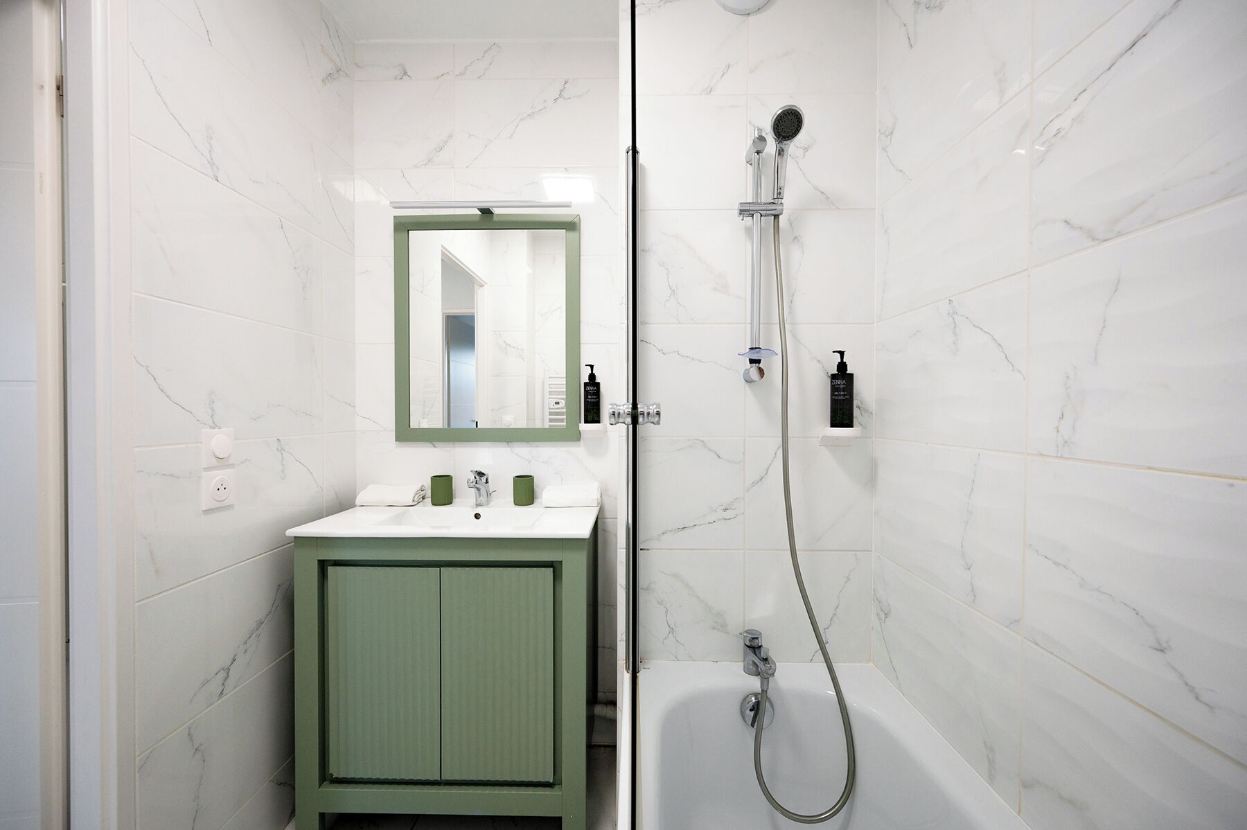 Une salle de bain avec un mur en marbre blanc, un meuble vert, un lavabo blanc, un miroir, une douche et une baignoire.