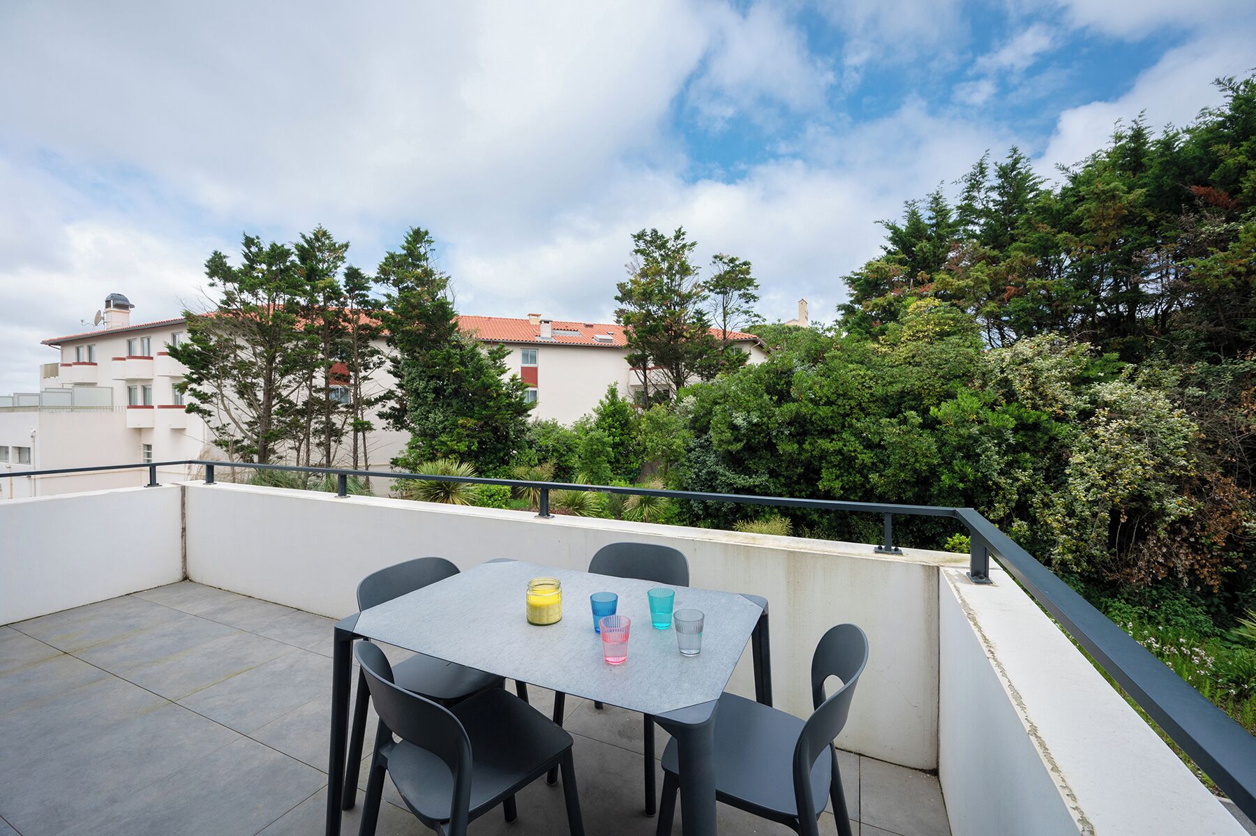 Una terraza en la azotea con una mesa y sillas, con vistas a una zona residencial con árboles y edificios.