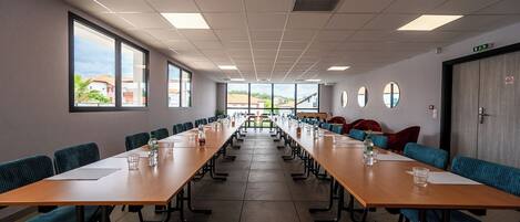 A conference room with long tables and chairs, large windows, and a view of buildings outside.