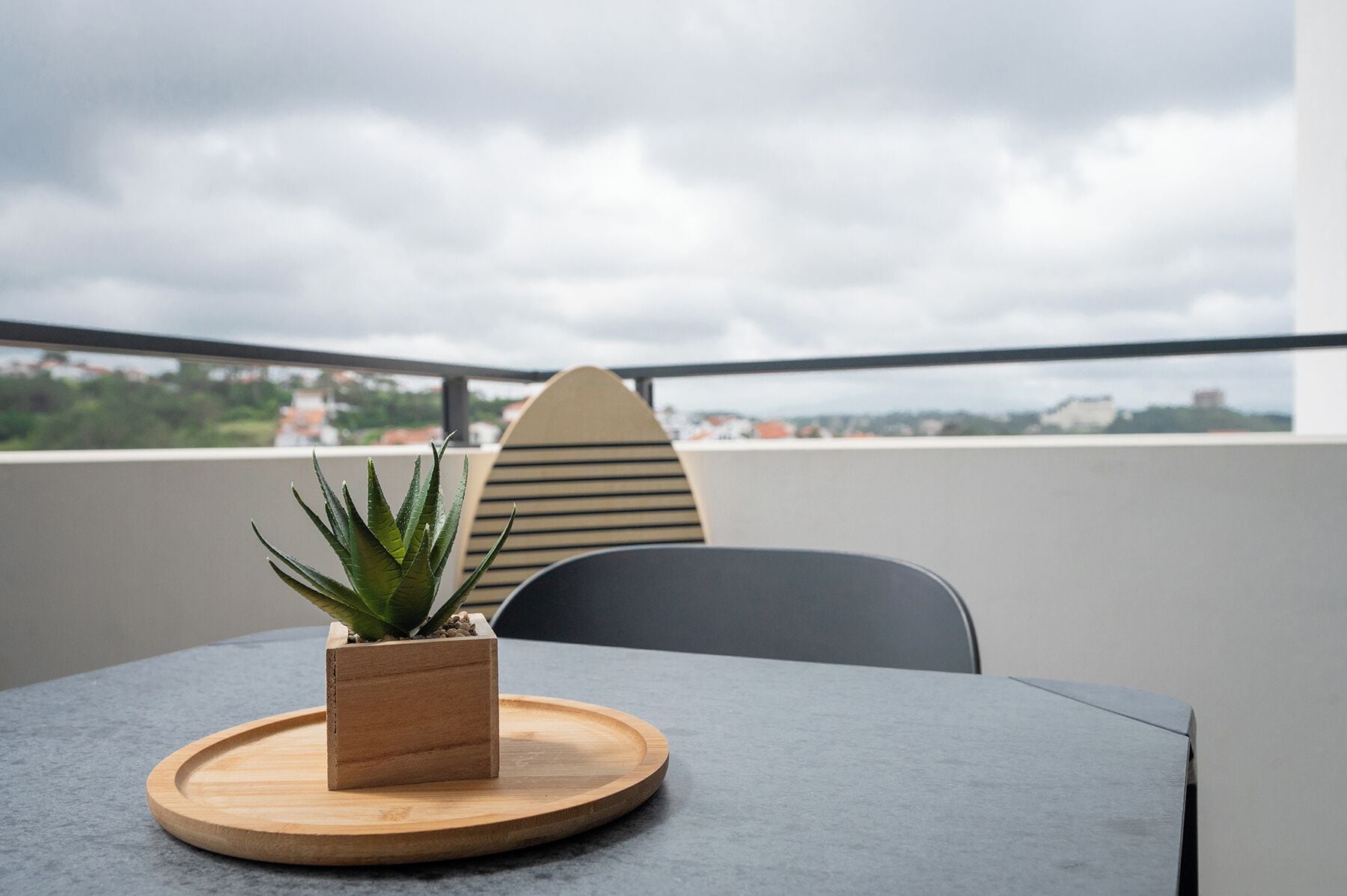 A table with a wooden tray and a potted plant on a balcony with a view of the city.