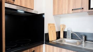 Una cocina moderna con tope de inducción negro, armarios de madera, un lavamanos de acero inoxidable y tablas de cortar de madera.
