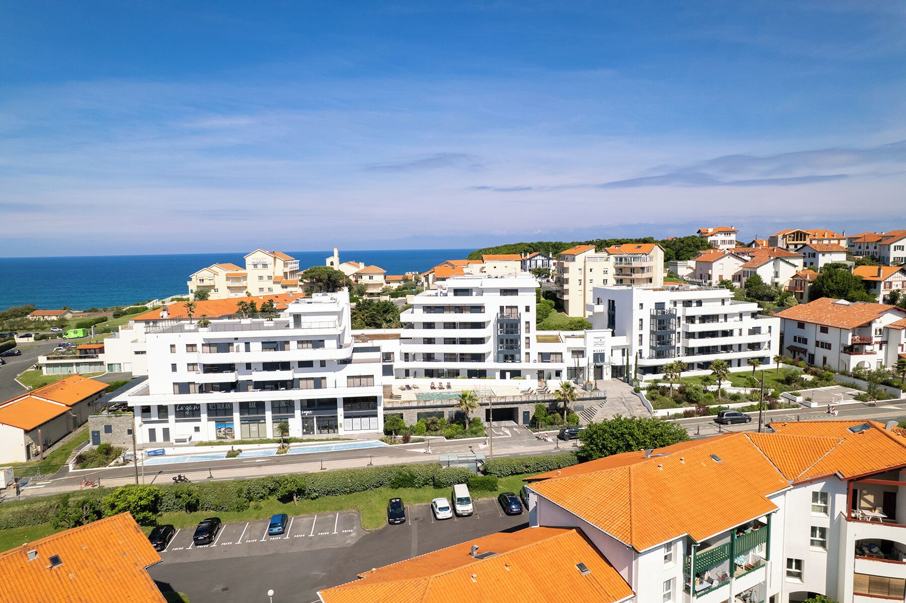 A coastal hotel with multiple floors, a swimming pool, and a view of the sea.