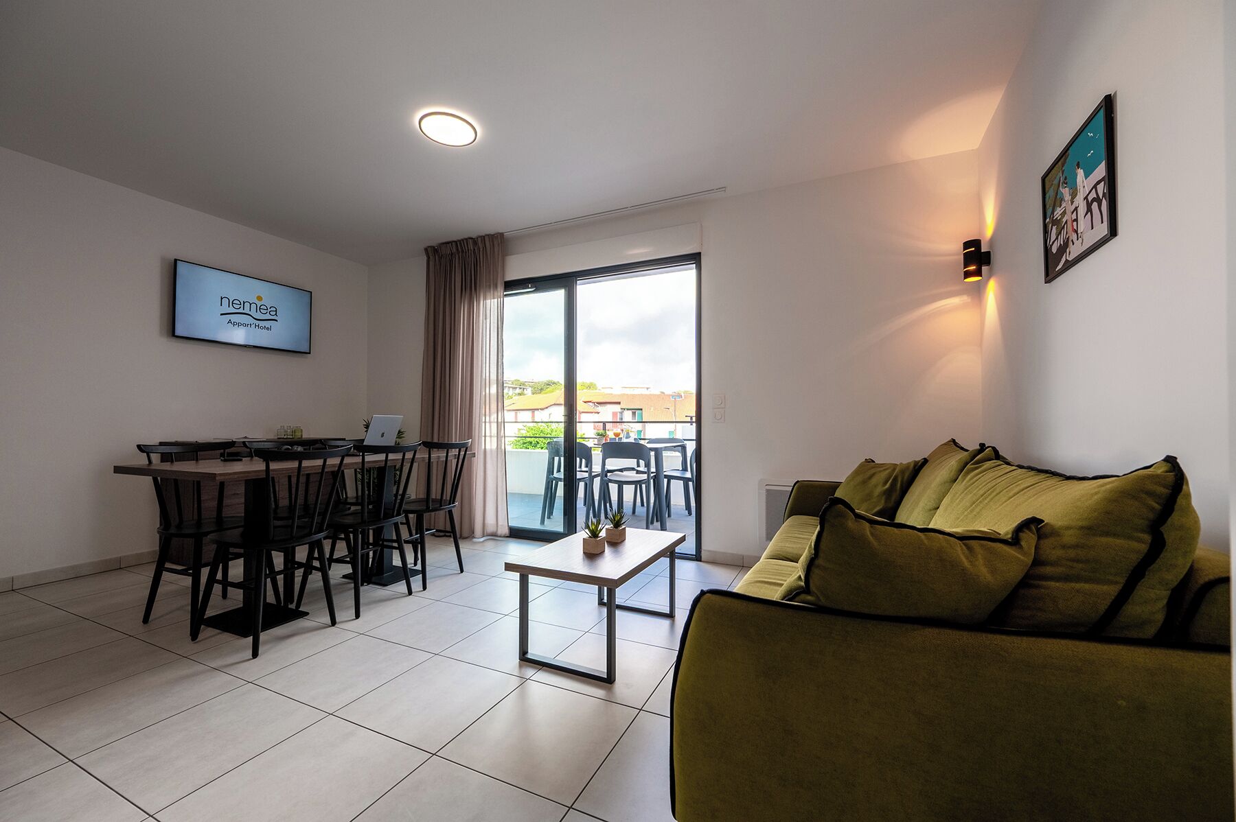 Una sala de estar moderna con un sofá, una mesa de comedor con sillas, una computadora portátil y un ventanal con cortinas.