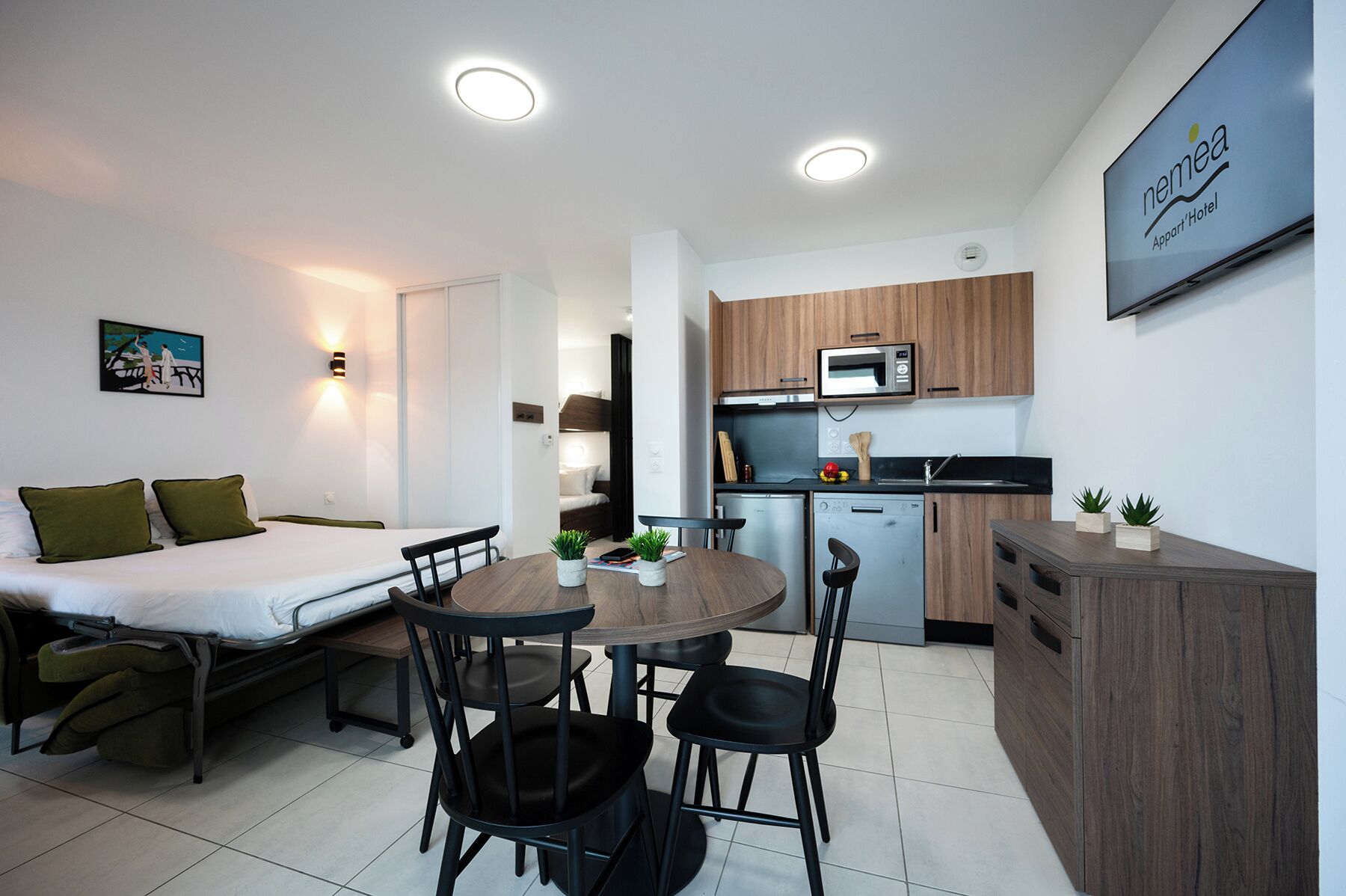 Habitación de hotel pequeña con cama, mesita de noche y una zona de comedor con sillas y mesa.