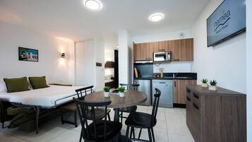 Habitación de hotel pequeña con cama, mesita de noche y una zona de comedor con sillas y mesa.