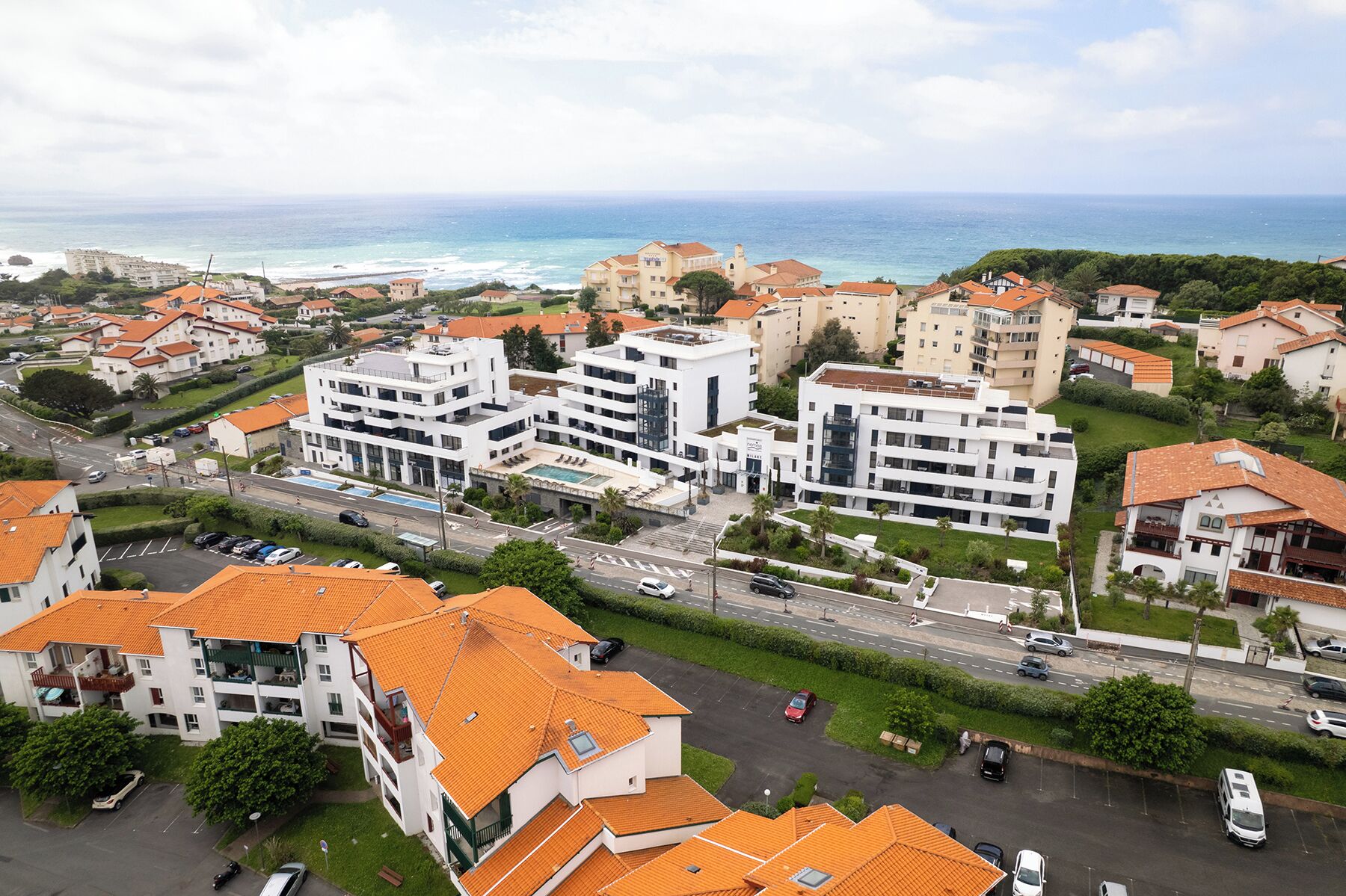 A coastal residential area with modern white buildings, a main road, and a view of the sea.