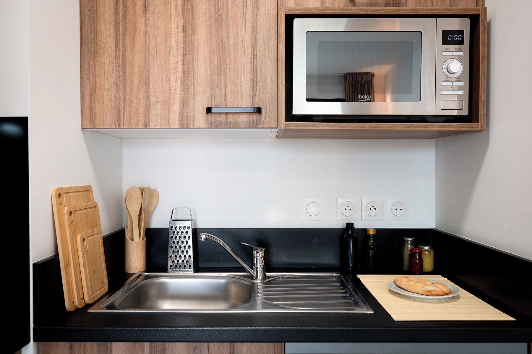 Una cocina moderna con un lavamanos de acero inoxidable, armarios de madera, un microondas y una tabla de cortar con una hogaza de pan.