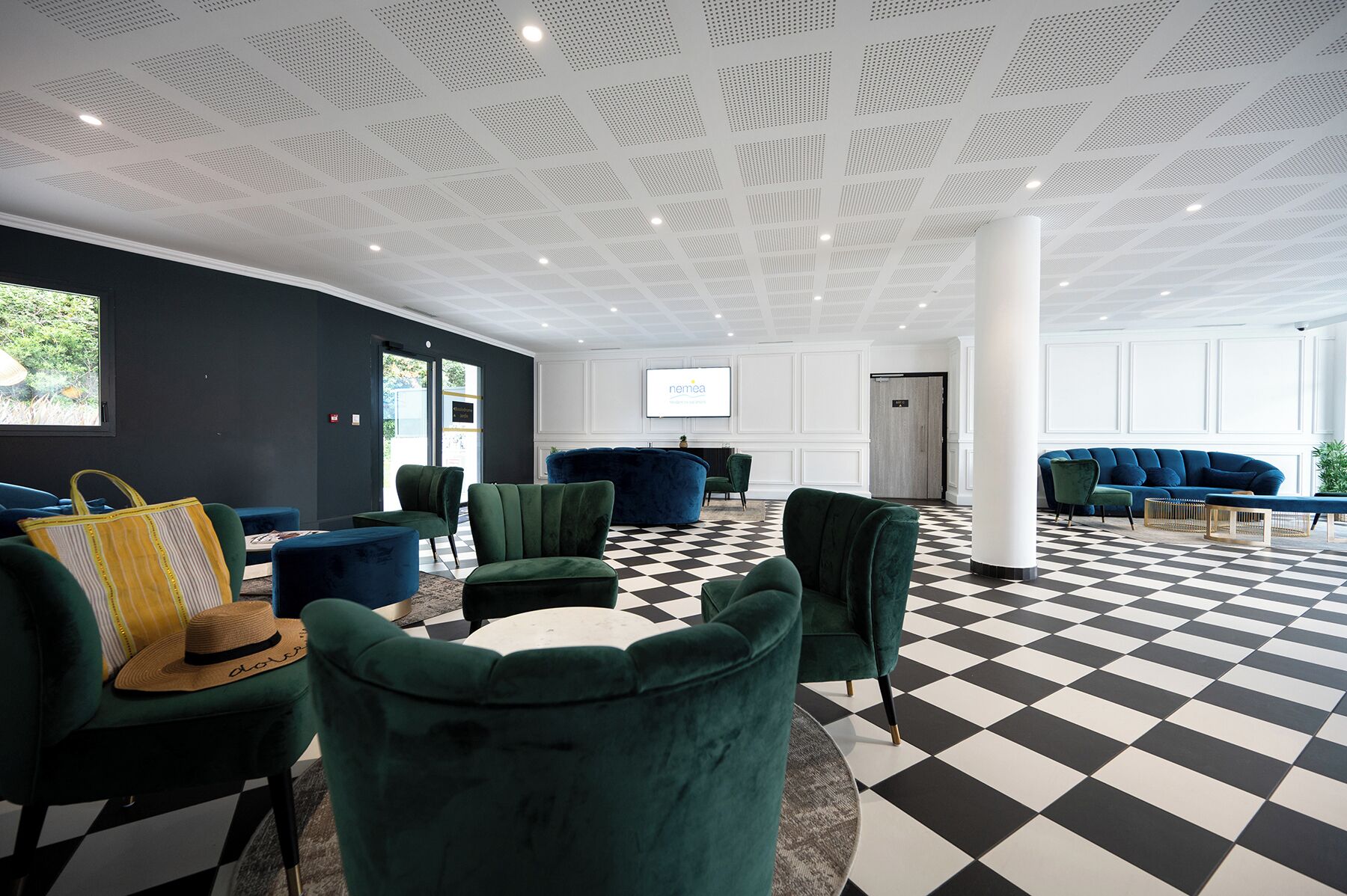 A modern lobby with green upholstered seating, a checkered floor, and a white ceiling with perforated panels.