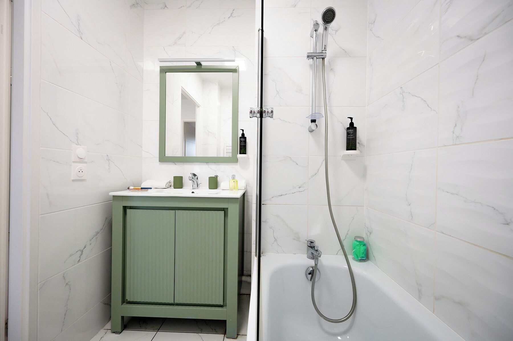 Un baño con tocador verde, un espejo, ducha con cabezal de ducha manual y bañera.