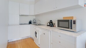 A compact kitchen with white cabinets, a washing machine, a microwave, and a sink. - Funchal View Apartment (Funchal)