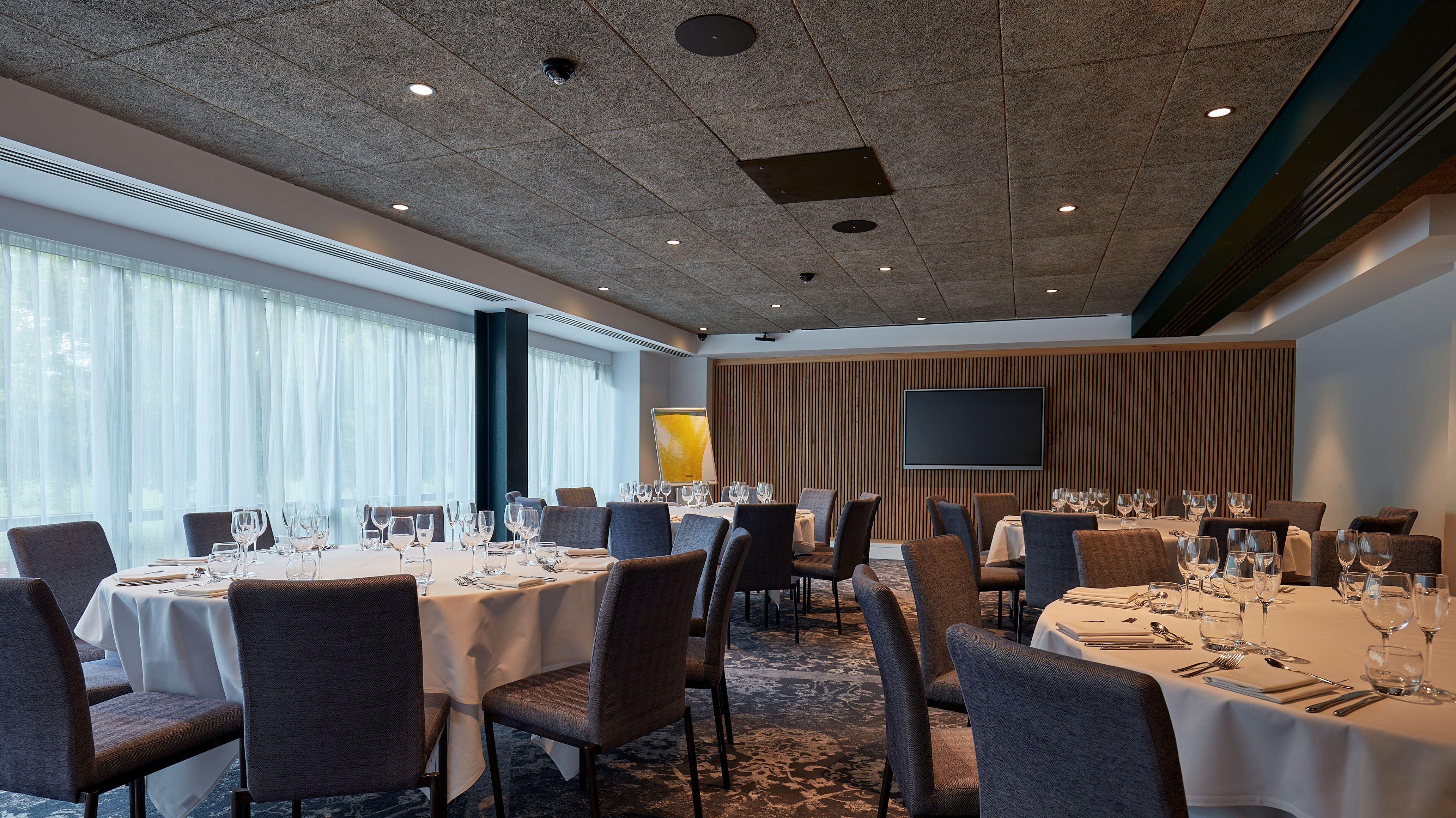 A conference room with round tables, chairs, and a large flat-screen TV on the wall.