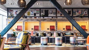 A modern lobby with a high ceiling, exposed brick walls, and a central staircase. There are seating areas with colorful cushions and a wooden reception desk. - voco Leicester by IHG (Leicester)