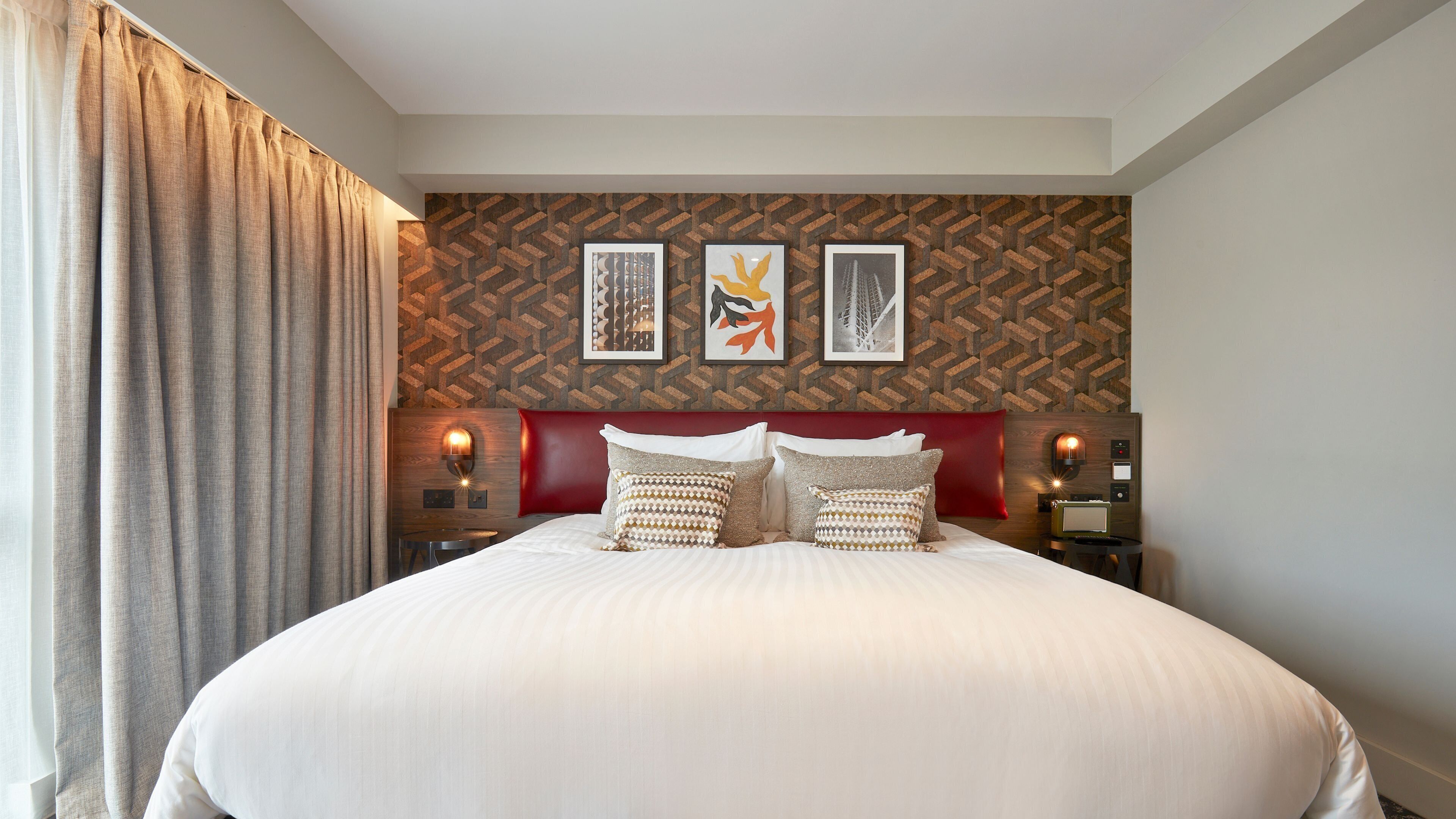 A large bed with a red headboard, multiple pillows, and a wall with geometric patterned wallpaper.