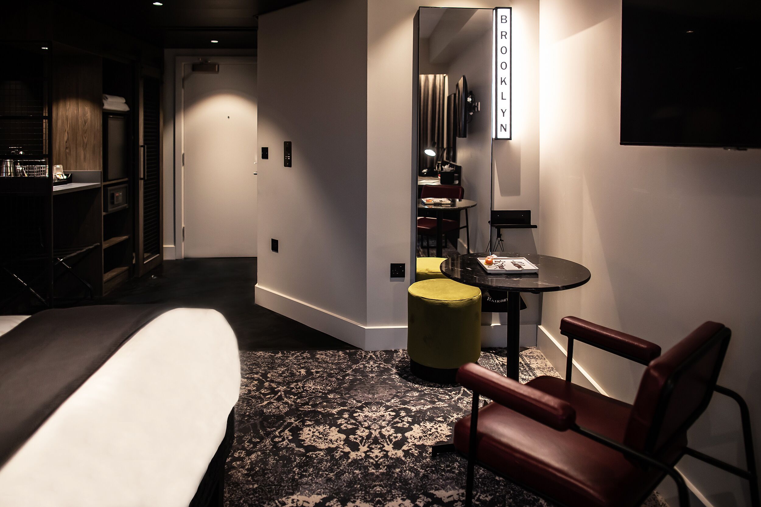 A hotel room with a bed, a desk, a chair, a small table, and a mirror.