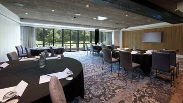 A conference room with tables, chairs, and a large screen.