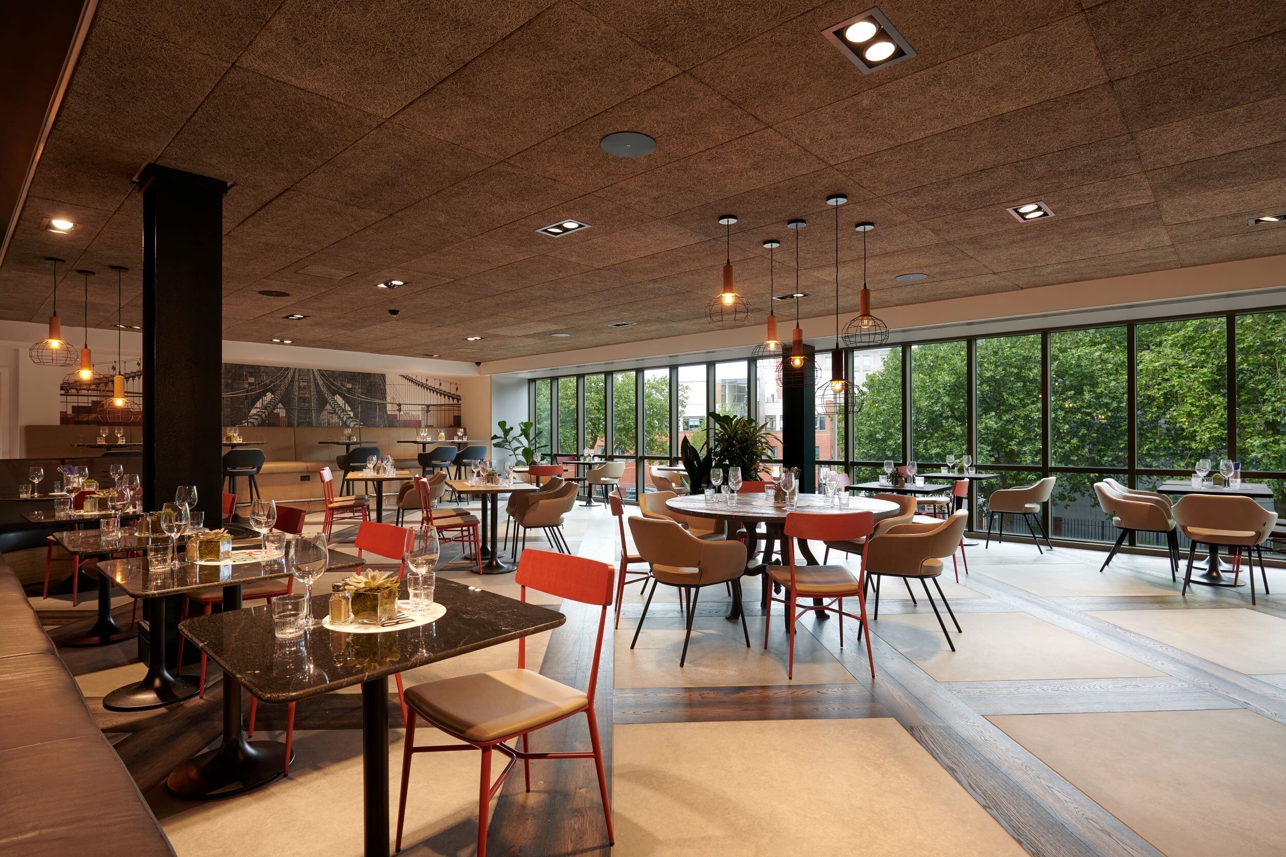 A spacious restaurant with high ceilings, large windows, and modern furnishings.