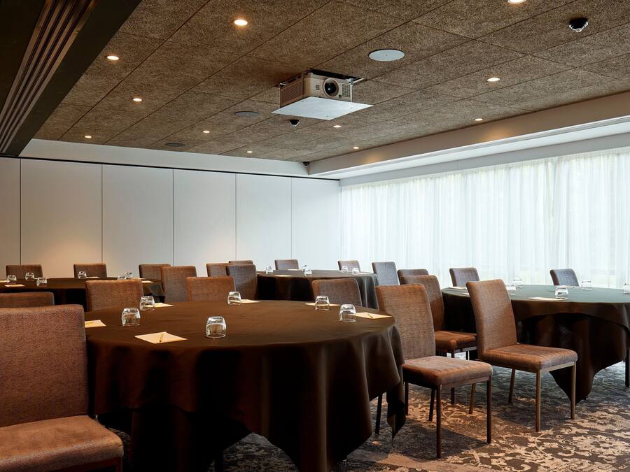 Uma sala de conferências com várias mesas e cadeiras, equipada com projetores e câmeras no teto.