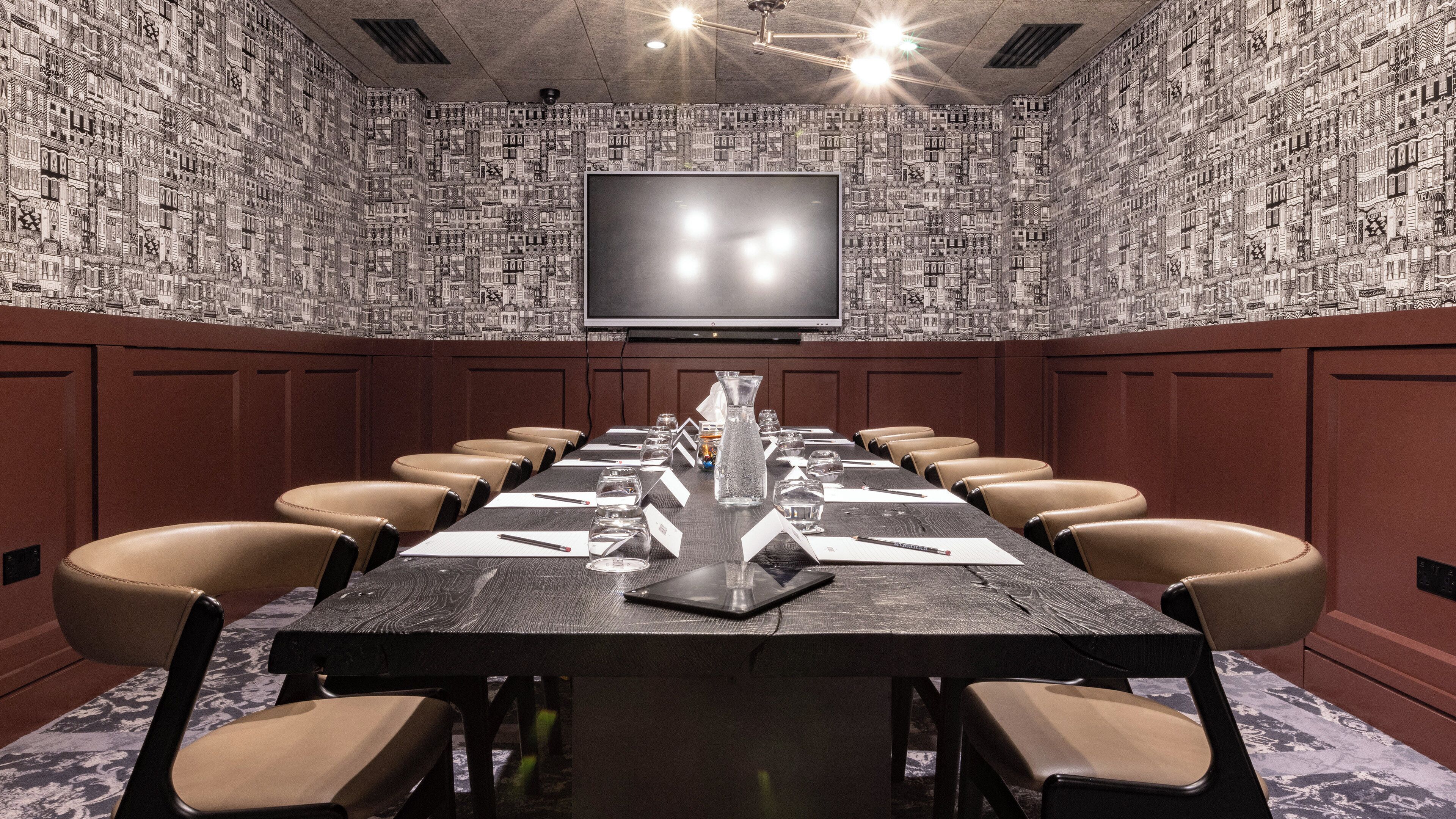 A conference room with a long table, chairs, a TV screen, and a patterned wall.
