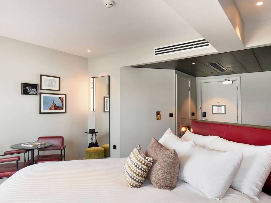 Ein Hotelzimmer mit einem großen Bett, einem Schreibtisch, einem Sessel, einem Fernseher und einem Spiegel.