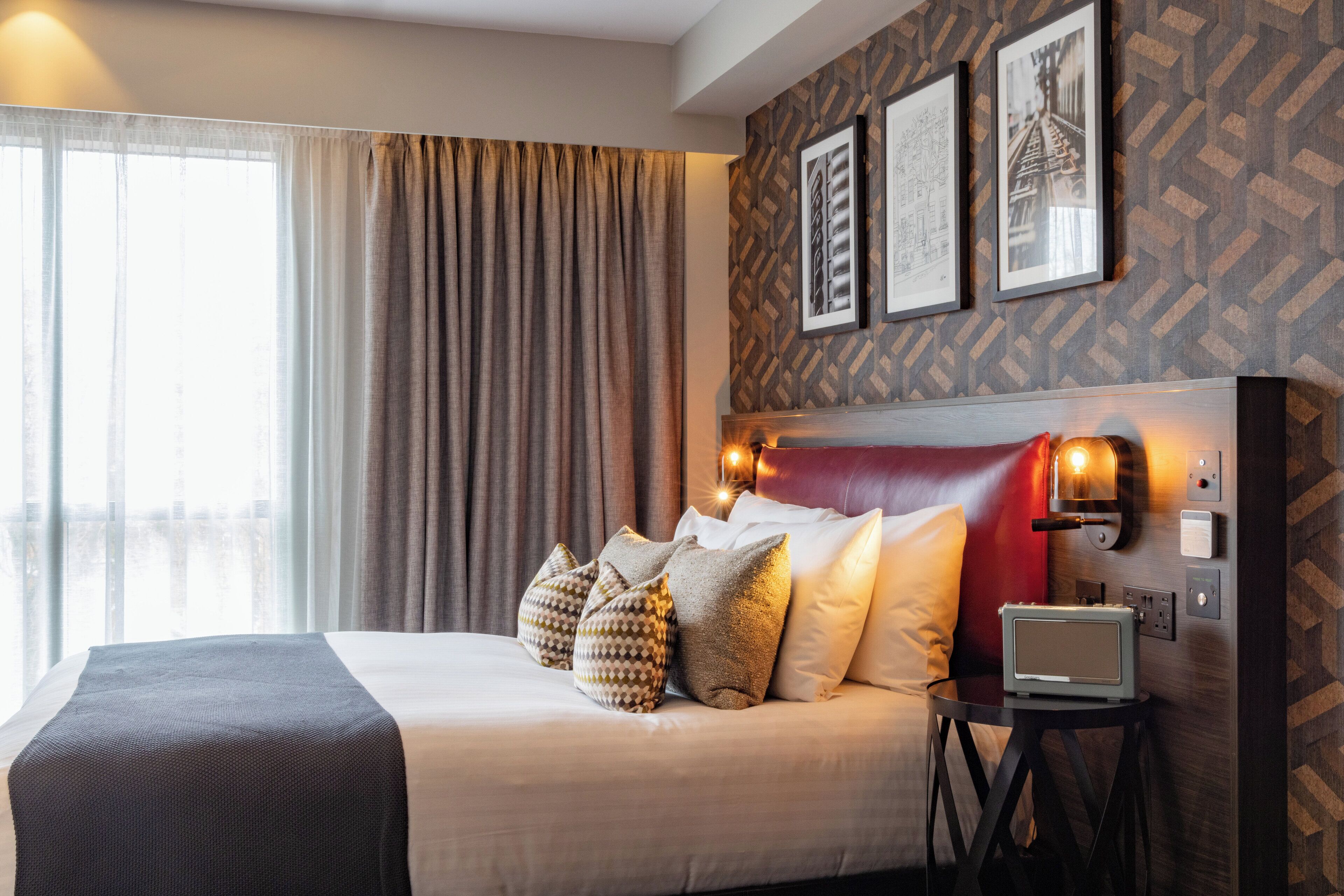 Une chambre d’hôtel avec un grand lit, une table de chevet avec une radio et une vue sur la ville par la fenêtre.
