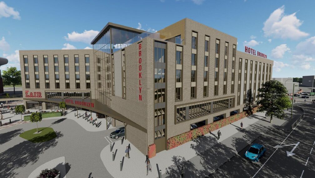Un moderno edificio de hotel con un llamativo letrero 'HOTEL BROOKLYN', varios pisos y un estacionamiento con automóviles.