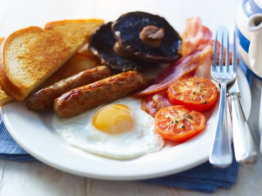 Une assiette de nourriture pour le petit-déjeuner comprenant des toasts, des saucisses, du bacon, des œufs et des tomates.