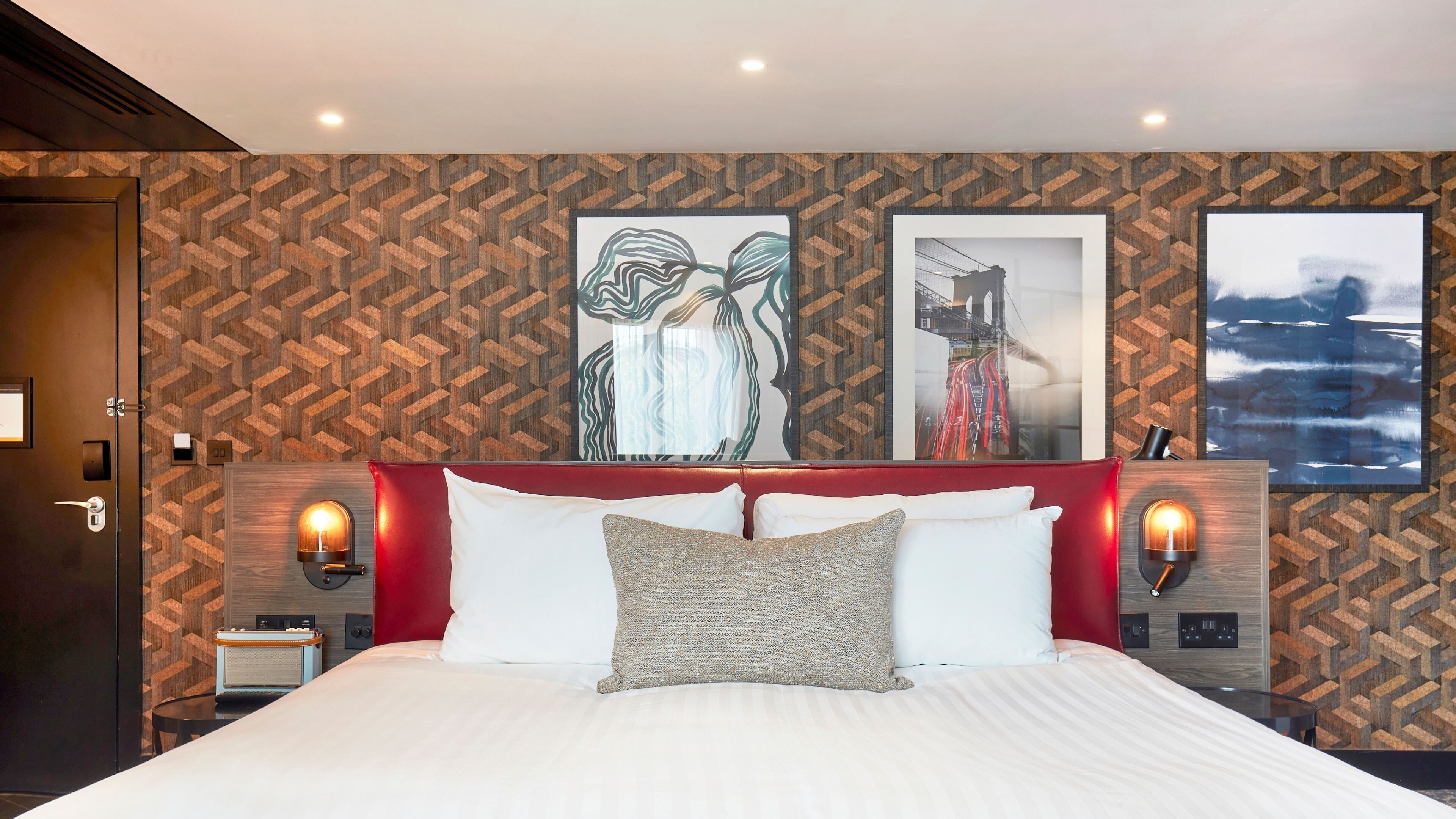 A hotel room with a large bed, two wall-mounted lamps, and three framed artworks on the wall.
