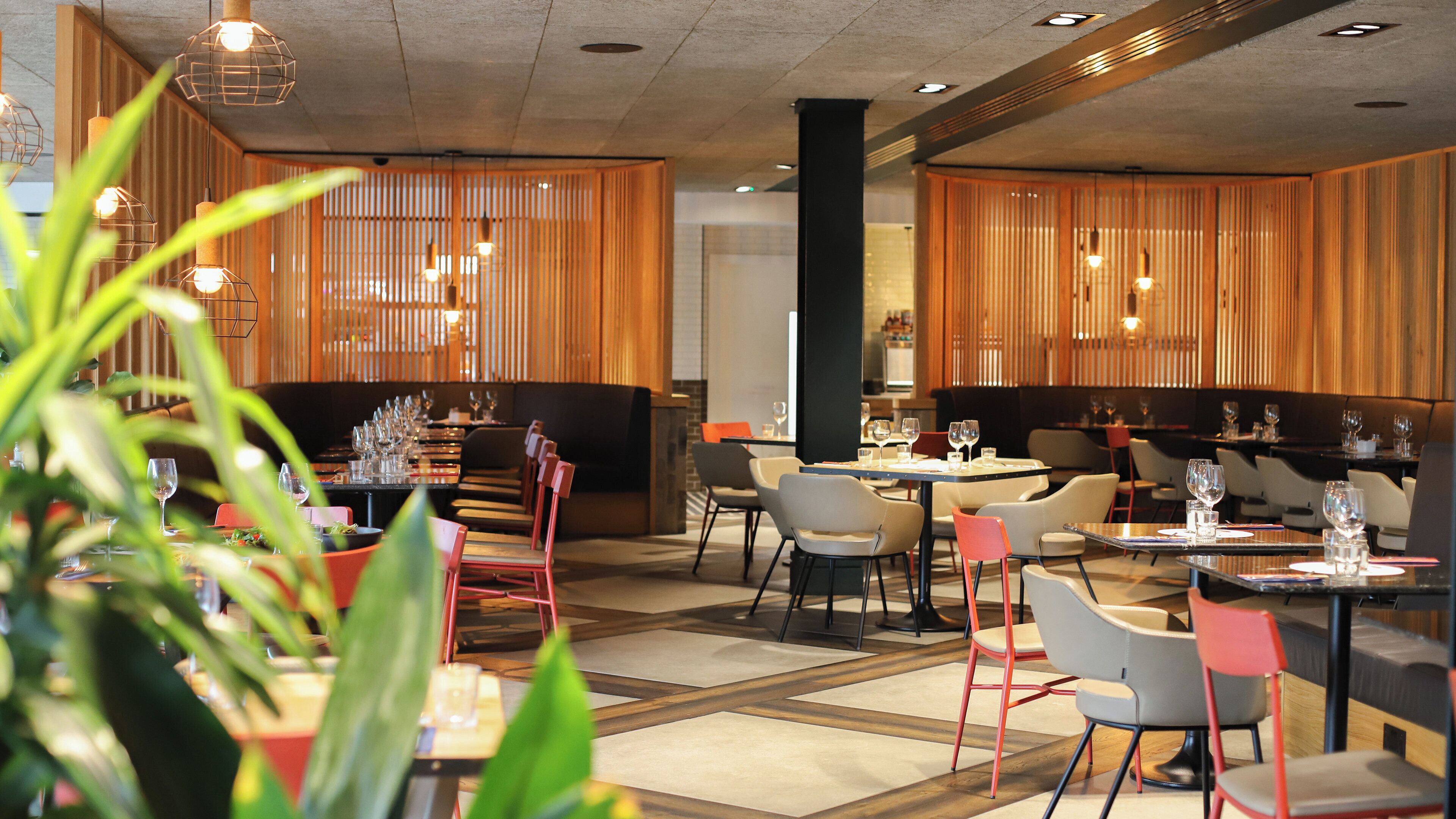 A restaurant with multiple tables and chairs, wooden paneling on the walls, and hanging pendant lights.