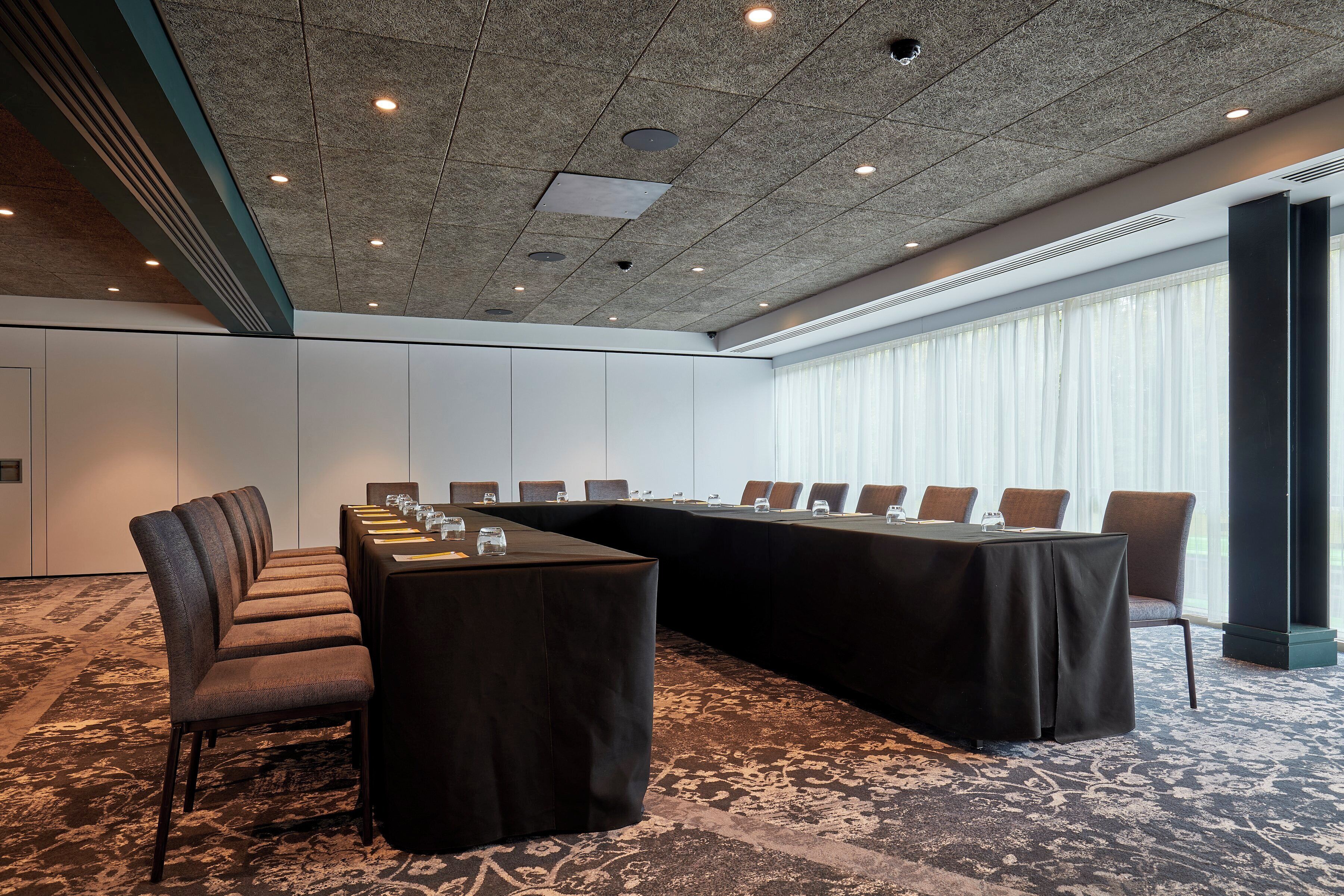 A conference room with a long table, multiple chairs, and a carpeted floor.