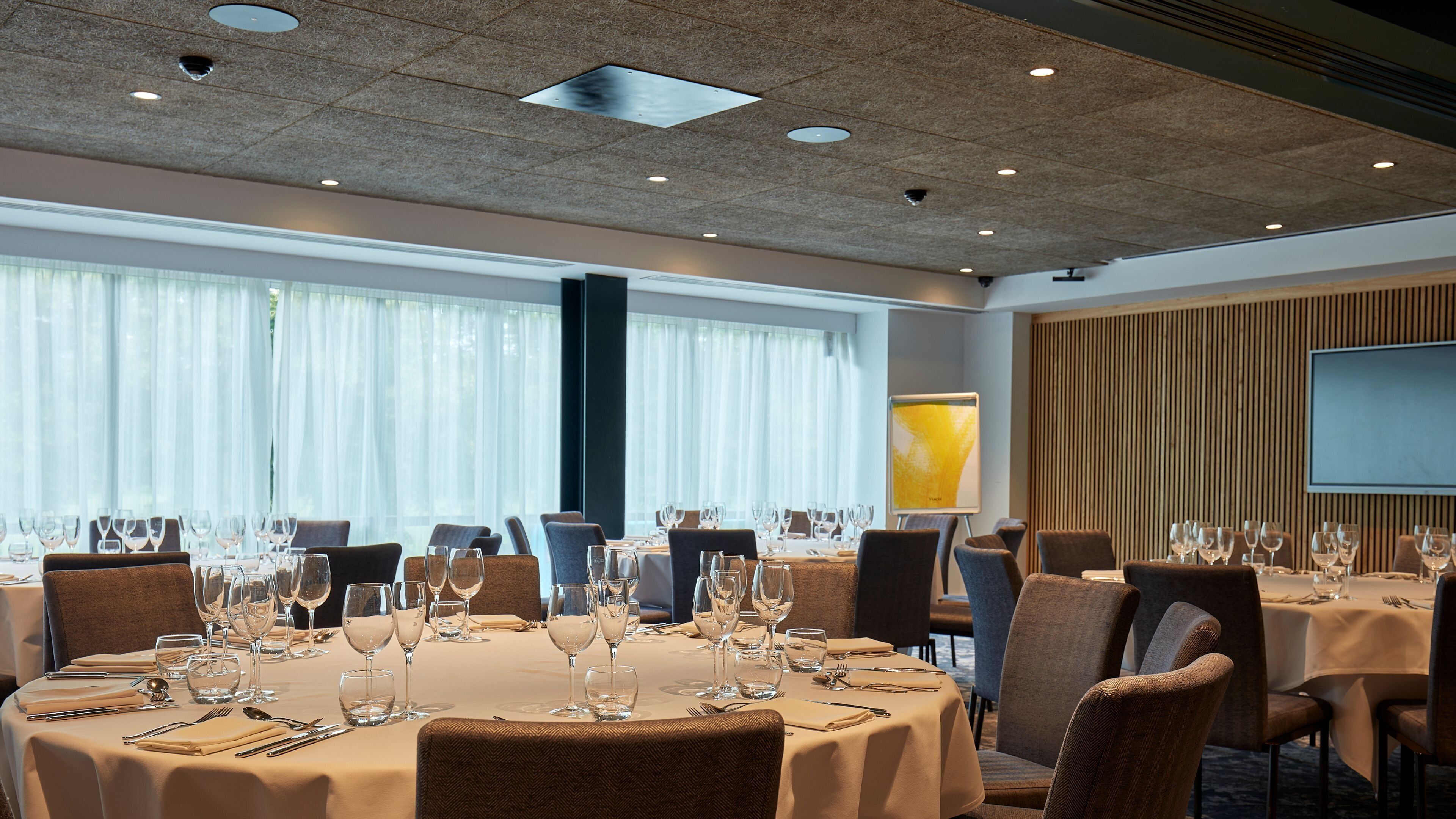 A conference room with round tables, chairs, and a large screen.