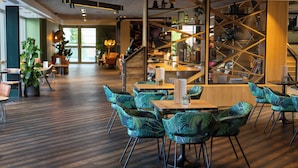 A modern cafe with wooden tables and chairs, a staircase with a geometric design, and potted plants. - voco Leicester by IHG (Leicester)
