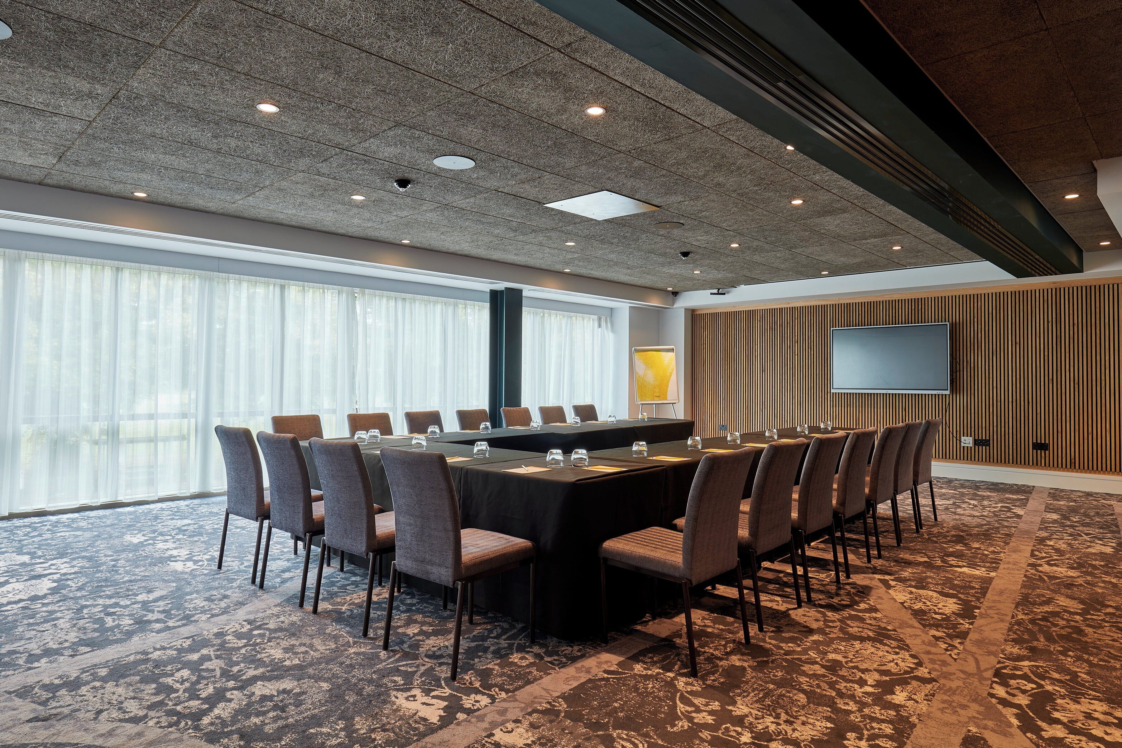 A conference room with a long table, chairs, a large screen, and a patterned carpet.