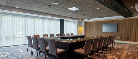 A conference room with a long table, chairs, a large screen, and a patterned carpet.