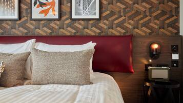 Una cama bien tendida con sábanas blancas y almohadones decorativos, cabecera roja y papel tapiz con diseño geométrico.