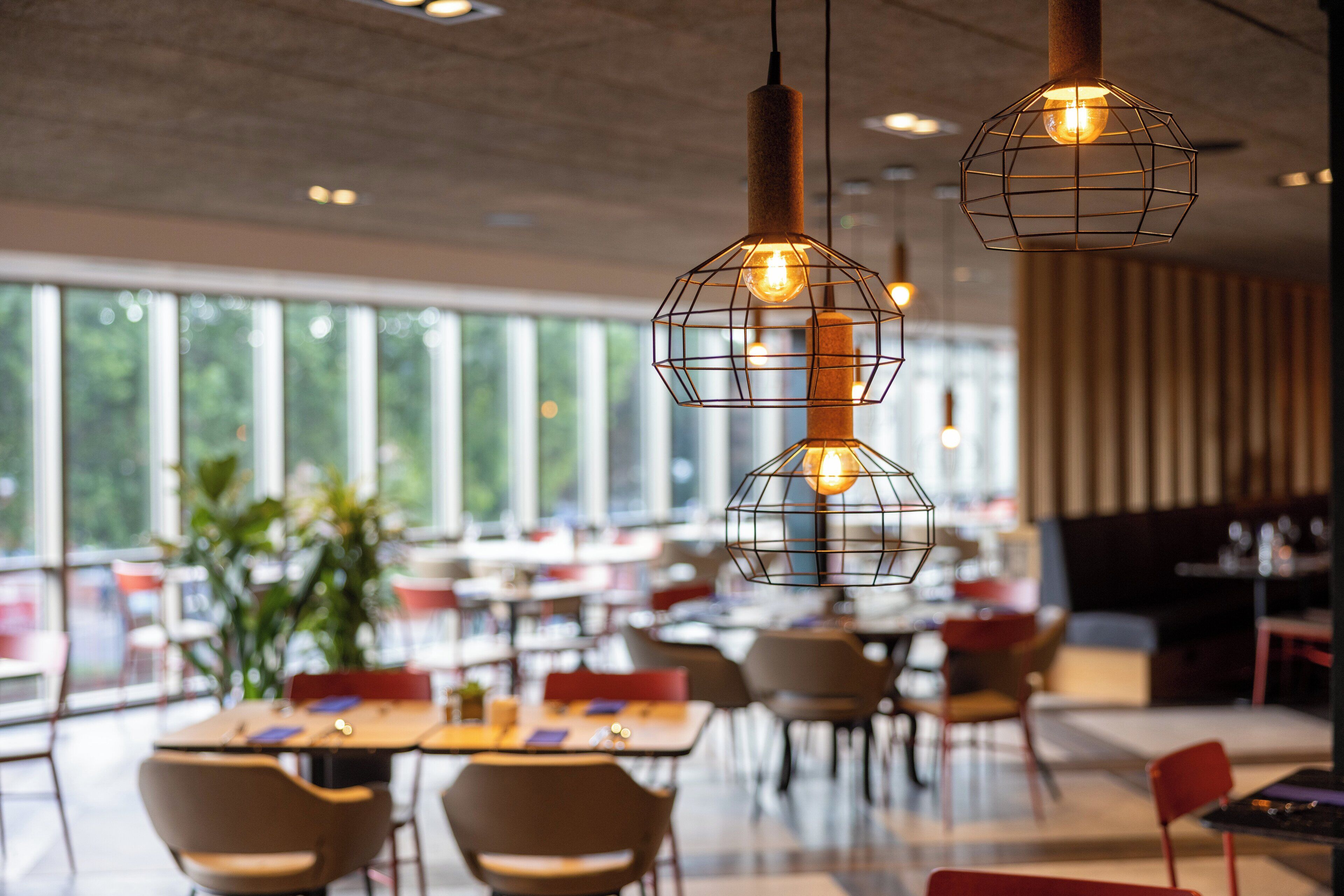A modern dining area with tables and chairs, large windows, and hanging pendant lights.