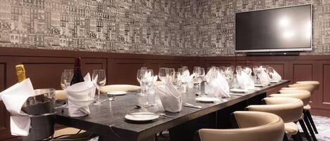 A conference room with a long table set for a meeting, a large screen on the wall, and a patterned wallpaper.