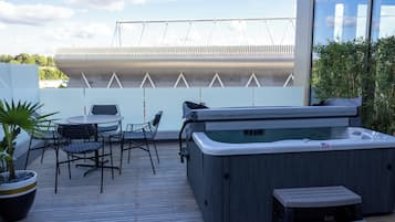 An outdoor deck with a hot tub, a table with chairs, and a potted plant.
