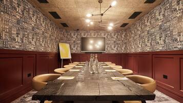 Un salón de conferencias con una larga mesa, varias sillas, una pantalla de proyector y un papel tapiz estampado en la pared.