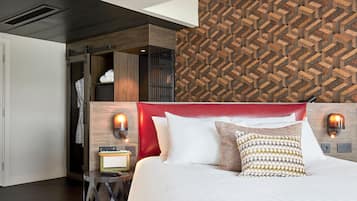 Una habitación de hotel moderna con un cabecero tapizado rojo, una pared de madera con un diseño geométrico y una cama con ropa blanca y almohadas estampadas.