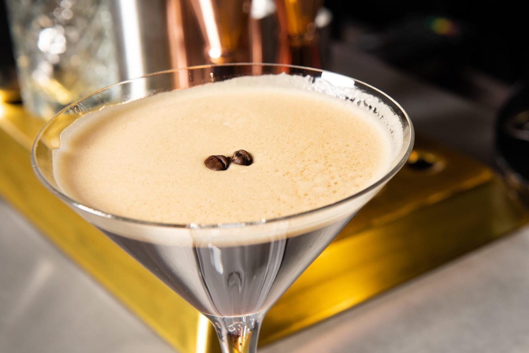 A martini glass with a frothy drink and two coffee beans on top.