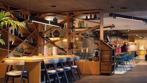 A modern bar area with a wooden bar counter, multiple chairs, and shelves with various items. - voco Leicester by IHG (Leicester)
