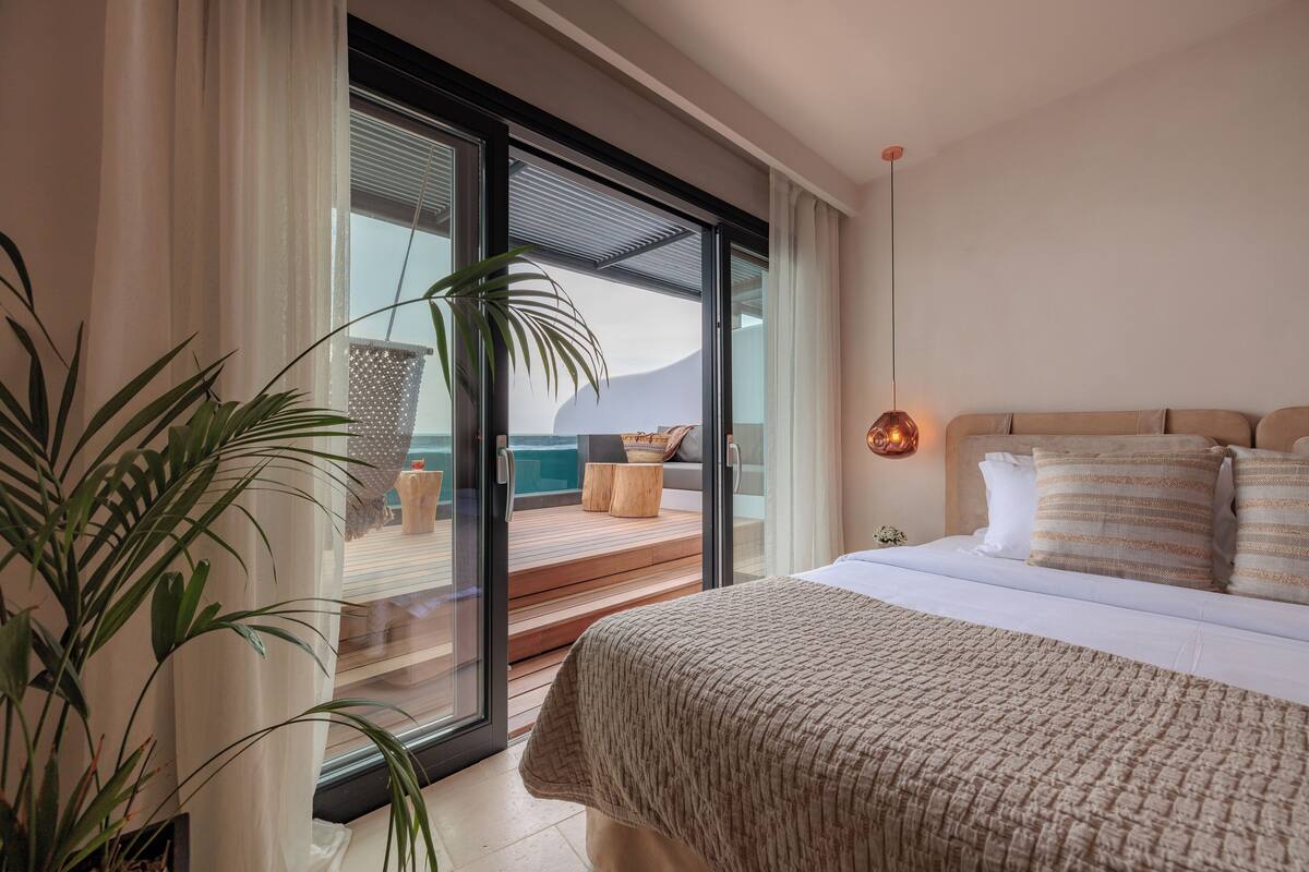 Un dormitorio con una cama grande, una puerta corrediza de vidrio a un balcón y una planta en maceta.