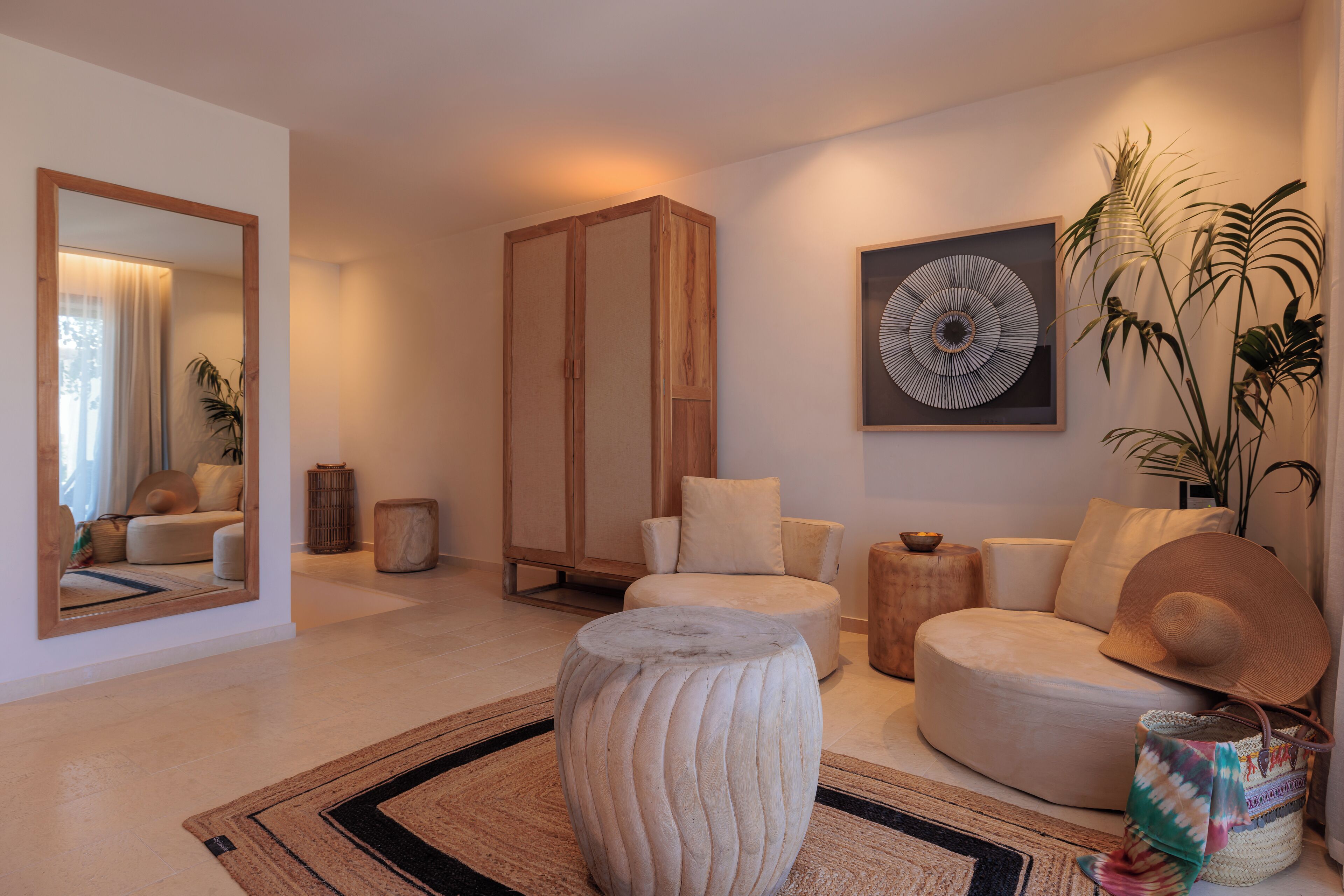 A modern living room with a large mirror, a round coffee table, a beige sofa, and a decorative wall piece.