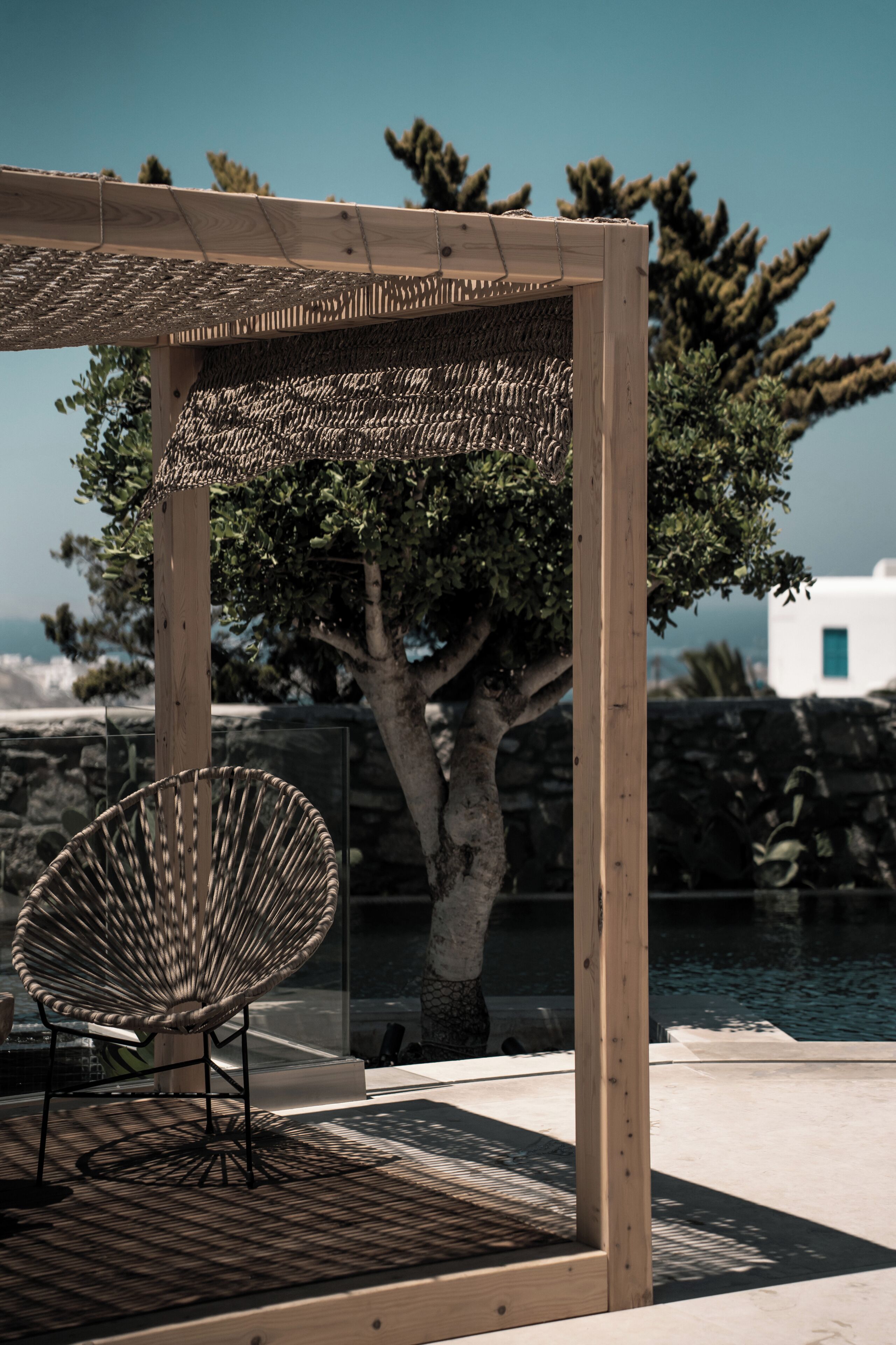 A wooden pergola with a woven ceiling, a wicker chair, and a tree in the background.
